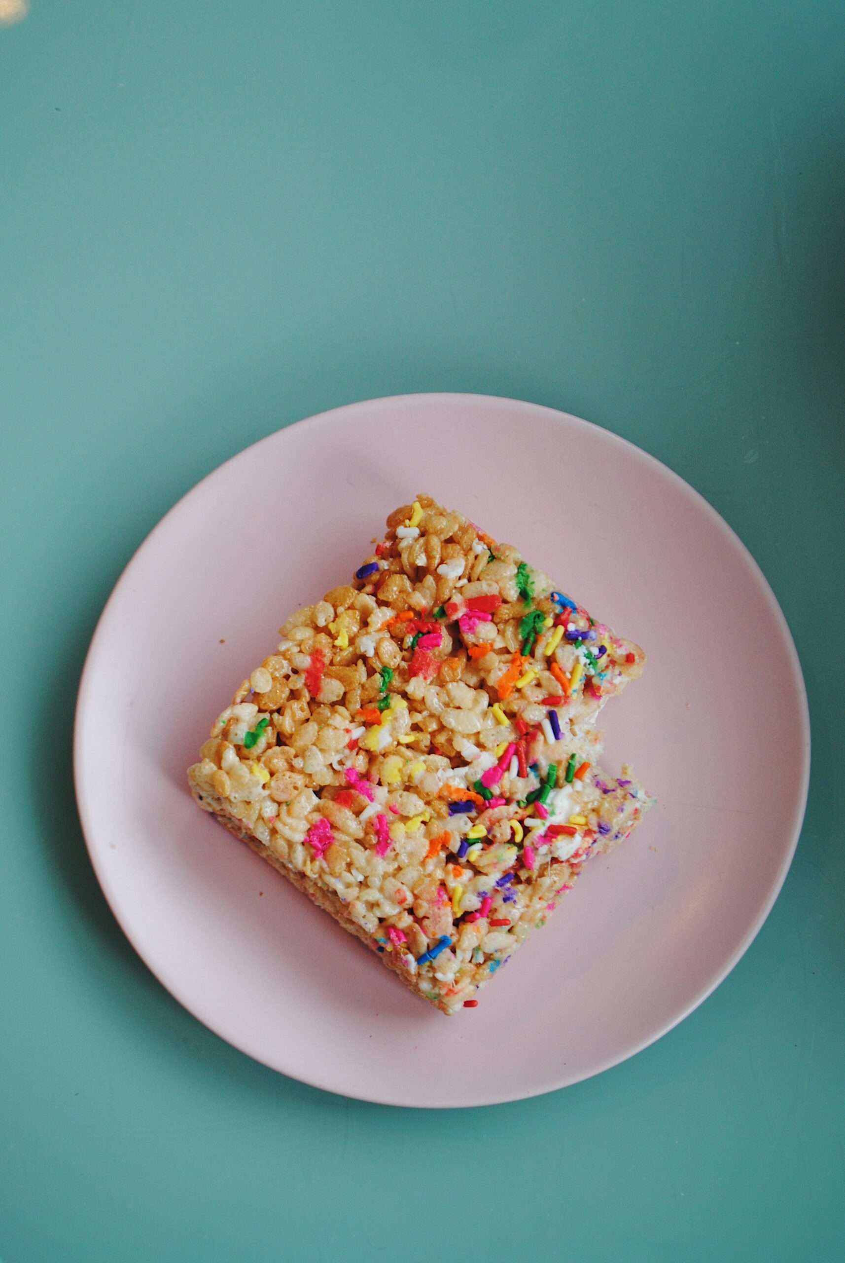 A rice krispy treat on a pink plate on top of a blue table.