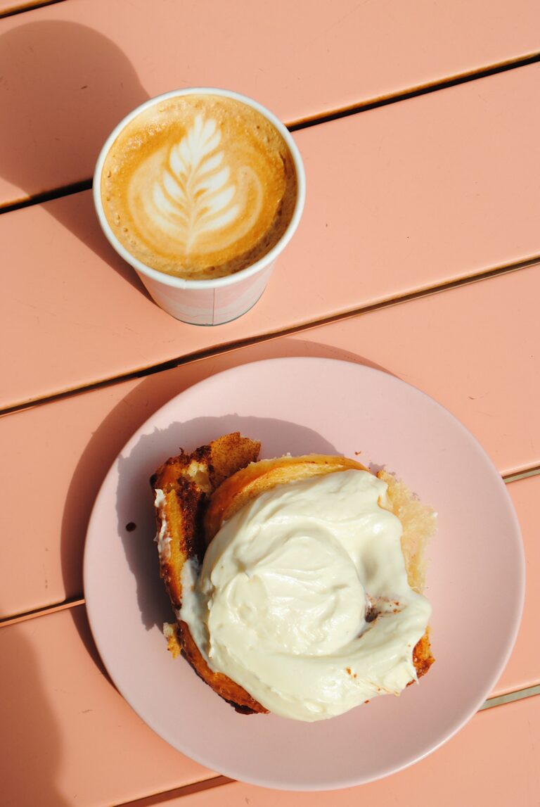 An aerial shot of a latte with leaf milk art and a cinnamon bun on a pink plate.