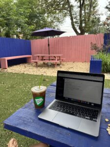 Alex taking a photo of her iced Vietnamese red eye next to her laptop on a picnic table. 